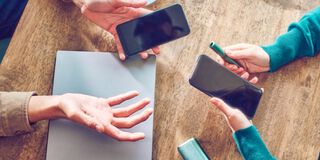 Hands holding smartphones and one IQOS device.