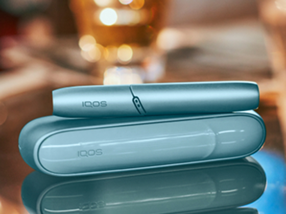 Laptop next to turquoise IQOS ORIGINALS DUO pocket charger.