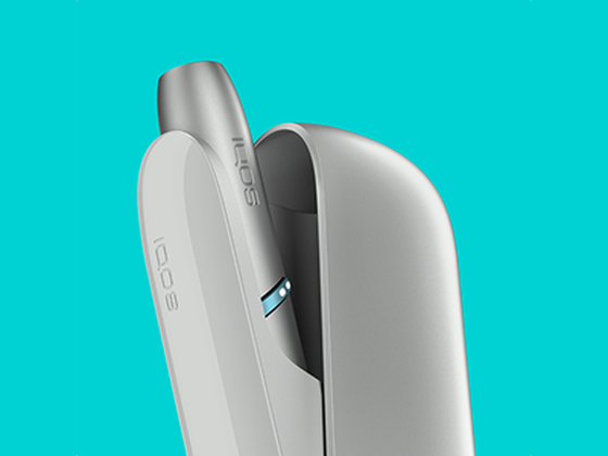 Laptop next to turquoise IQOS ORIGINALS DUO pocket charger.