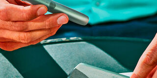 A woman sitting at a table next to her suitcase with a smartphone, passport and plane ticket.