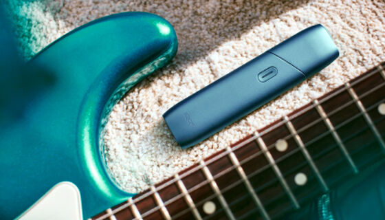 IQOS Originals One device next to turquoise headphones.