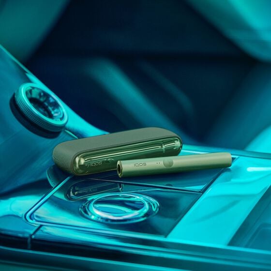 A man holding an obsidian black IQOS ILUMA PRIME Holder while looking at his mobile phone.