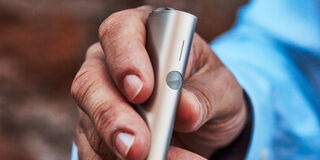 Hands holding smartphones and one IQOS device.